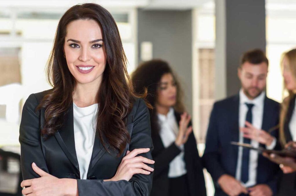 Donna al lavoro sorridente. Sullo sfondo un team di persone che parlano