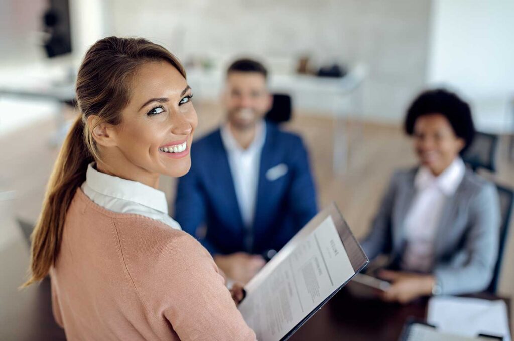 Donna sorridente a un incontro di lavoro con altre due persone